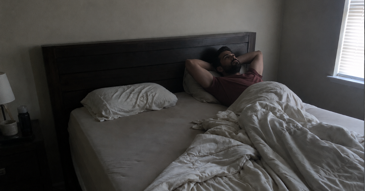 A person lying awake at night lit by their phone while their partner sleeps turned away in the dark.